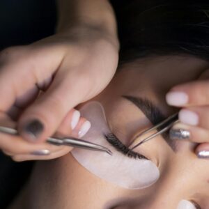 Detailed view of a beautician applying eyelash extensions to a woman's eyes.
